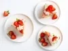 Fotografia em tons claros de três pratos brancos sobre uma mesa off white. Dentro dos pratos rasos tem uma fatia da sobremesa, super consistente, com pedaços de morango em cada prato.