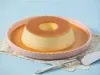 Imagem de um prato rosa claro com um pudim de leite condensado moça com calda de caramelo.