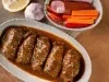 Em cima de uma mesa, refratário com bifes suculentos enrolados com molho de tomate, decorado com ervas.