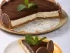 Em cima de uma mesa, prato redondo com fatia de torta de biscoitos calipso, com creme branco e ganache de chocolate.
