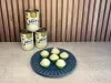Seis brigadeiros brancos em forminhas verdes sobre prato azul, com três latas de LEITE MOÇA® ao fundo.