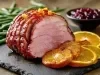 Fotografai em tons claros de de um tender fatiado, no ponto, com cinco fatias caramelizadas de laranja, sobre um apoio preto retangular.