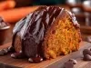 Fotografia de uma fatia de bolo de cenoura, com textura rica e cobertura de ganache de chocolate, e rodeada por cenouras e mais chocolate.