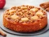Fotografia de um bolo de maçã e nozes, com crosta dourada e cobertura de caramelo, decorado com pedaços de maçã e nozes inteiras, em um prato escuro, cercado por canela e anis estrelado.