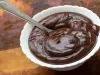 Fotografia de um recipiente pequeno branco fundo com brigadeiro de whey. O recipiente está sobre uma mesa de madeira.