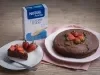 Foto da receita de bolo cremoso de aveia servida em um prato disforme branco com outro prato ao lado servido de uma fatia do mesmo bolo, tudo isso sobre um pano cor de rosa em cima de uma mesa de madeira
