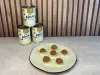 Seis brigadeiros em prato claro diante de três latas de LEITE MOÇA® sobre bancada e painel de madeira.