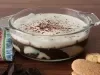 Em cima de uma mesa, recipiente redondo de vidro com creme de chocolate, decorado com chantilly e raspas de chocolate.
