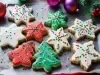 Em cima de uma mesa, prato com biscoitos em formato de estrelas e árvores de Natal, decorados com glacê colorido e confeitos coloridos de bolinhas verde e vermelho.