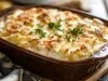 Em cima de uma mesa, recipiente com bacalhau cremoso gratinado com queijo, decorado com cheiro-verde picado.