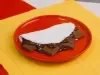 Tapioca dobrada recheada com creme de chocolate e pedaços de Baton, servida em prato vermelho.
