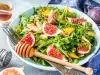 Em cima de uma mesa, prato com salada com mix de folhas, frutas em cubos e figo.