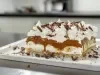 Em cima de uma mesa, prato com fatia de banoffee com massa crocante, chantilly com doce de leite e bananas em rodelas, decorado com chantilly e raspas de chocolate.