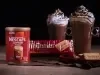 Foto da receita de cappuccino crocante servida em duas canecas altas de vidro sobre uma mesa de madeira