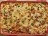 Foto bem aproximada de uma travessa vermelha, dentro da qual está a receita de Arroz de Forno, decorada com ervilhas e peito de peru