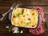 Em cima de uma mesa, refratário com batatas com queijo gratinado com molho branco, decorado com alecrim.