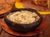 Em cima de uma mesa, há um refratário redondo queijo gratinado por cima.