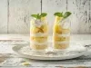 Fotografia em tons claros de dois copos longos com a sobremesa em camadas com pedaços de abacaxi, decorados com chantilly e hortelã.