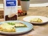 Fotografia em tons de marrom com um prato azul ao centro. Em cima do prato existe uma pizza com massa de Aveia coberta com queijo muçarela e orégano. Ao fundo existe uma embalagem de Farelo de Aveia NESTLÉ.