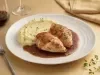 Pedaços de frango dourados servidos com purê cremoso de batata e molho escuro reduzido, apresentados em prato branco elegante