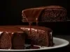 Um bolo de chocolate inteiro com cobertura de ganache brilhante. Um pedaço foi cortado e está sendo servido, revelando o interior macio e bem assado. A calda escorre de forma apetitosa pela fatia e pelas bordas do bolo.