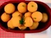 Fotografia vista de cima de bolinhas de queijo dentor de um recipiente oval marrom de vidro sobre um pano vermelho quadriculado com branco, o qual está apoaido em uma mesa branca.