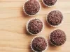 Fotografia vista de cima de seis brigadeiros passados no granulado dentro de uma forminha branca sobre uma tábua de madeira clara.