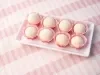 Imagem de uma travessa retangular branca sobre uma toalha listrada rosa claro, com docinhos de leite ninho em forminhas vermelhas com branco.