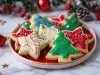 Em cima de uma mesa, prato redondo com biscoitos em formatos de estrela e árvore de natal, decorados com glacê colorido e confeitos de bolinhas coloridas.