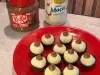 Docinhos cobertos com coco ralado em prato vermelho, decorados com creme de KitKat e Leite Moça ao fundo.