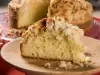 Fotografia de uma receita de cuca alemã tradicional com uma fatia grande cortada sobre um prato raso de madeira. No fundo tem a receita quase inteira sobre um apoio de vidro raso.