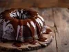 Fotografia de bolo de chocolate em forma de bundt, coberto com um brilho de chocolate que escorre pelas laterais. O bolo está sobre uma superfície de madeira rústica.