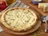 Fotografia em tons de azul em uma bancada de madeira, um pano azul listrado, uma tábua de madeira de pizza, um cortador de pizza ao lado e pedaços de queijo.