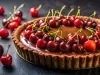 Fotografia em tons escuros de uma torta de chocolate e amarenas sobre uma mesa preta. Ao redor tem cerejas inteiras e também sobre a torta.