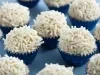 Fotografia em tons de branco e azul de vários brigadeiros em forminhas azuis metalizadas com granulado branco.