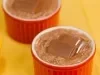 Cocada cremosa em ramequim vermelho, coberta com pedaço de chocolate recheado, sobre toalha amarela.