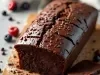 Bolo de chocolate cremoso em uma tábua de madeira, com cobertura brilhante e raspas de chocolate. Uma fatia foi cortada, revelando um interior denso.