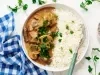 Imagem vista de cima de um prato branco com arroz e strogonoff de carne bem cremoso. Ao lado, um paninho xadrez azul e folhas de salsinha decorando.
