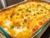 Em cima de uma mesa, refratário com batatas com queijo gratinado, decorado com cheiro-verde picado.