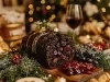 Fotografia de um bolo de chocolate com frutas secas fofinho, decorado com uma fita dourada, cercado por ramos de pinheiro e frutas vermelhas.