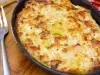 Em cima de uma mesa, refratário preto com queijo gratinado, ao lado, garfo.