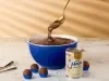 Fotografia mostra um pote cheio de brigadeiro. Alguns brigadeiros em forminhas azuis em volta e a lata de leite moça.