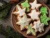 Em cima de uma mesa, prato redondo com biscoitos em forma de estrelas, decorado com glacê branco e verde, e confeitos redondos brancos.