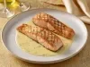Filés de salmão grelhados servidos com molho cremoso claro e ervas, apresentados em prato raso com acabamento sofisticado.