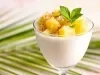 Fotografia em tons claros de uma taça de vidro com o creme de abacaxi e cubos de abacaxi mais caramelizados com folhas de hortelã por cima.