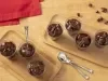 Fotografia vista de cima de duas mini tábuas de madeira, levemente fundas, retangulares, sobre uma mesa de madeira clara. Apoiado nas tábuas tem alguns copinho de acrílico com brigadeiro cremoso de nescau.