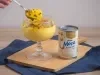 Foto da receita de Mousse de maracujá feita com o suco concentrado da fruta, servida em taças de vidro, com uma decoração de calda de maracujá com sementes, sobre uma tábua de madeira e ao lado de uma lata de Leite Moça