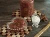 Fotografia em tons escuros de uma mesa de madeira escura. Sobre a mesa tem dois apoios quadriculados de madeira, apoiado em um deles tem um pote de vidro com doce de banana. No outro apoio tem o doce num pote de vidro pequeno em formato de coração.