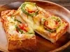 Fotografia de um pão pizza de queijo deretido com tomate, cortado na metade e a outra metade esta apoiado sobre a outra metade. As metades estão em um prato redondo de madeira raso.