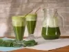 Fotografia em tons de verde com dois copos grandes ao centro. Dentro dos copos existe uma receita de suco verde feita com couve e Molico.